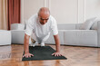 © Alina Hvostikova/Stocksy - Positive aged man doing plank exercise at home