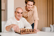© Alina Hvostikova/Stocksy - Happy senior man with son playing chess at home