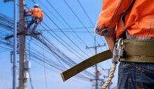 Midsection Of Electrician Lineman Wearing Safety Belt With Blurred Background Of Electrical Workers Team Are Working On Power Poles In Public Area