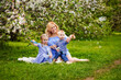 © Elena  - A happy family of blonds. Chubby mom and two kids boy and girl in a blooming spring apple orchard on a spring picnic. They start blowing soap bubbles.