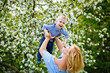 © Elena  - Mom and son in a blooming apple orchard in spring. A woman holds a child in her arms, plays and has fun with it.
