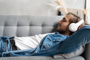 Middle aged man listening music with headphones relaxed in sofa at his home.