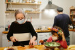 © Jimena Roquero/Stocksy - Grandmother and granddaughter preparing a salad in the kitchen wearing face masks.