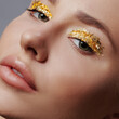 © Elena Kharichkina/Stocksy - Portrait of beautiful young woman with long blond hair and fashion make-up, Gold glitter on face