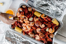A Hand Reaching For Crawfish / Crayfish And Boiled Shrimp And Corn