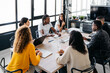 © Sergio Marcos/Stocksy - Group of multiracial businesspeople sitting around table having a meeting in modern workplace