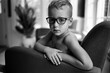 © Jakob Lagerstedt/Stocksy - Handsome young boy with eyeglasses and no shirt sitting in a chair