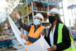 © Jimena Roquero/Stocksy - Construction worker reporting to woman engineer while holding some blueprints in front of the construction.