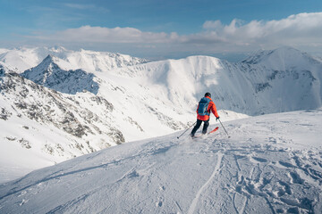 Skier rides freeride on powder snow down the slope against the backdrop of the mountains. A man is skiing down the hill on the steep slope