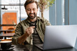 © Drobot Dean - Unshaven happy man using laptop and credit card while sitting in cafe