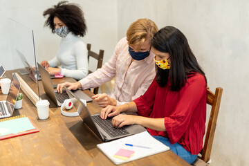 teamwork during Covid19 outbreak, multi-ethnic people working on their laptops in a co working space, man points at the screen and helps a woman with troubleshooting, university student collaboration