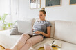 © Mihajlo Ckovric/Stocksy - Woman working from home using laptop while sitting on the sofa