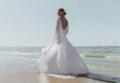 © Evgeniya Savina/Stocksy - A blonde haired woman standing with her back position on the beach wearing a long bridal gown