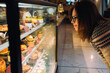 © Vradiy Art/Stocksy - Young woman looking on the showcase with different desserts in coffee shop