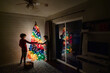 © Jennifer Bogle/Stocksy - Siblings decorate rainbow tree in dining room