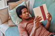 © Ivan Gener/Stocksy - Young man reading a book on his sofa