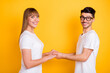 © deagreez - Photo of pretty cute young couple wear white t-shirt spectacles holding hands arms isolated yellow color background