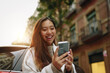 © MyMicrostock/Stocksy - Asian woman laughing while using a mobile phone