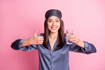 Sticker - Photo portrait of excited girl holding glass of water raising thumb up isolated on pastel pink colored background