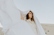 © Mango Street Lab/Stocksy - Girl with white jumpsuit standing on dunes with white sheet