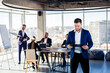 © Дмитрий Ткачук - Successful handsome male mentor, director, businessman in a suit at the office. Working day concept. Team meeting with the boss in the foreground