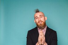 Bearded European Businessman In Dark Suit Isolated On Turquoise Background Begging And Praying With Hands Together With Hope Expression On Face Very Emotional And Worried