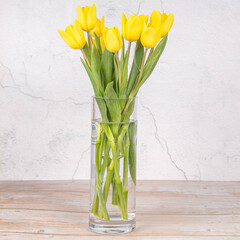 Wall Mural - Yellow flowers, tulips in a vase. On a light background. Congratulations on Easter. ER