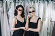© Alex Li - Beautiful girls in black dresses and black sunglasses, stands on the background of dresses hanging on a hanger.