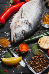 Wall Mural - Raw sea fish dorado with lemon, pepper, tomatoes and various spices. On a black rustic background.