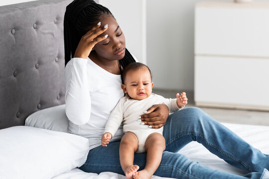Tired African American mom sitting with kid on bed