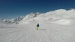 A man skiing down a perfectly groomed slope in Heiligenblut, Austria. He is wearing a green and blue winter outfit. High mountains around. Winter ski resort. Clear and sunny day. Winter wonderland
