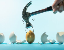 Intact Golden Egg Holds The Hammer Among Broken White Eggs. Funny Character. The Concept Of Reliability, Resistance To Adverse Conditions.