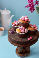 Muffins decorated with pink chocolate eggs. Easter muffin. Pink, blue, purple. Side view, blue background. Coffee, flowers.