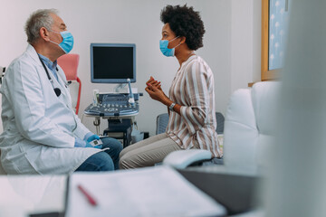 Wall Mural - Male doctor with face mask examining his female patient in clinic office