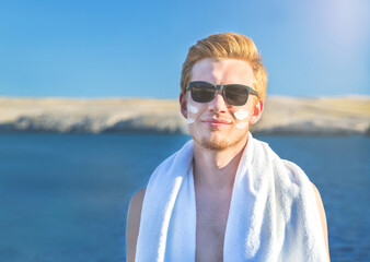 Wall Mural - Attractive man with protective sun cream (solar cream, sunscreen ) on the face for care of his body. Young handsome caucasian male model with red hair in sunglasses. Healthy skin.