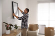 © New Africa - Man hanging picture on white wall in room. Interior design