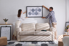 Happy Couple Hanging Picture On White Wall Together. Interior Design