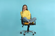 © New Africa - Young woman sitting in comfortable office chair on turquoise background