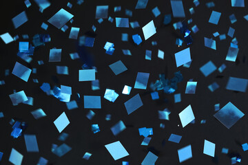 Shiny blue confetti falling down on black background