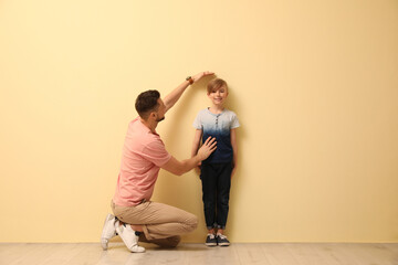 Wall Mural - Father measuring height of his son near beige wall indoors