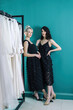 © Alex Li - Beautiful girls in black dresses, against the background of a beautiful wall. Designer clothing. The blonde is leaning back on a hanger with dresses.
