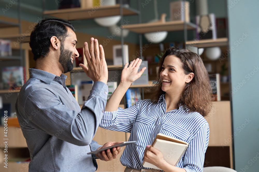 Two happy friendly diverse professionals, teacher and student giving high five standing in office celebrating success, good cooperation result, partnership teamwork and team motivation in office work. - obrazy, fototapety, plakaty 