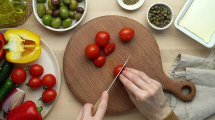 Wall Mural - Step by step recipe for greek salad horiatiki. Woman hands with knife, chopping tomatoes. Wooden board for cutting vegetables and ingredients. Homemade food, preparing meal at home kitchen, top view