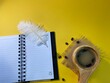 on a yellow background an open notebook with an Ostrich feather and next to it coffee in a wooden cup and scattered coffee beans