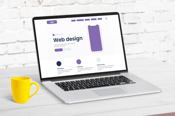 Wall Mural - Web design studio page concept with website elements on laptop computer. Clean desk with yellow coffee mug beside