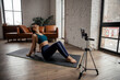 © Ankor_stock. - Young fit woman blogger in sportswear shoots video on phone as she does exercises at home in the living room.