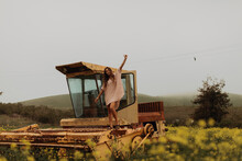 Young Woman In Field Of Yellow Wildflowers Standing On Top Of Abandoned Combine Harvester, Portrait, Jalama, California, USA