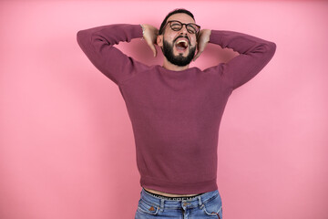 Handsome man wearing glasses and casual clothes over pink background relaxing and stretching, arms and hands behind head and neck smiling happy