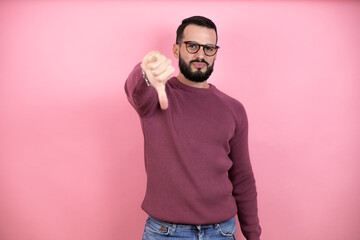 Wall Mural - Handsome man wearing glasses and casual clothes over pink background with angry face, negative sign showing dislike with thumbs down