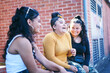 © Connect Images - Young woman and her teenage sisters sitting on wall laughing